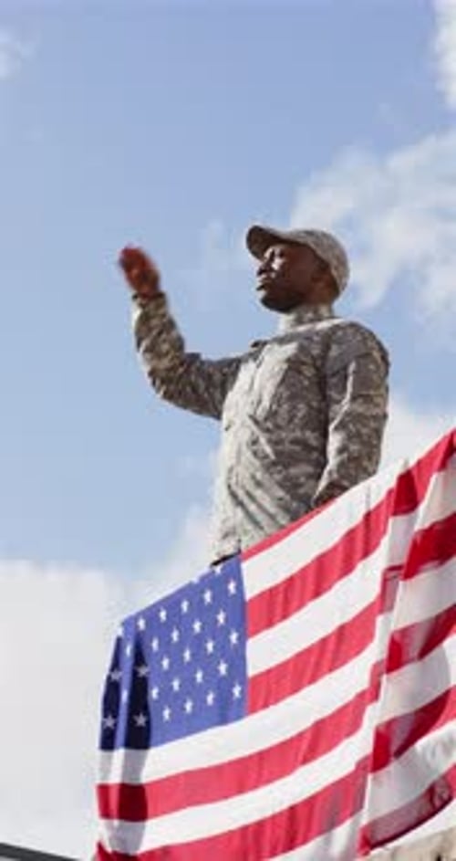 Vertical video: Saluting, soldier in uniform standing by American flag, showing patriotism