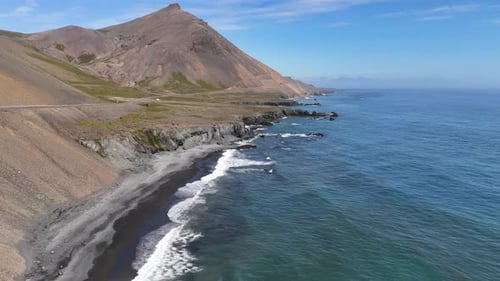 Aerial view of ocean waves hitting the rugged cliffside mountains of Iceland, revealing a winding