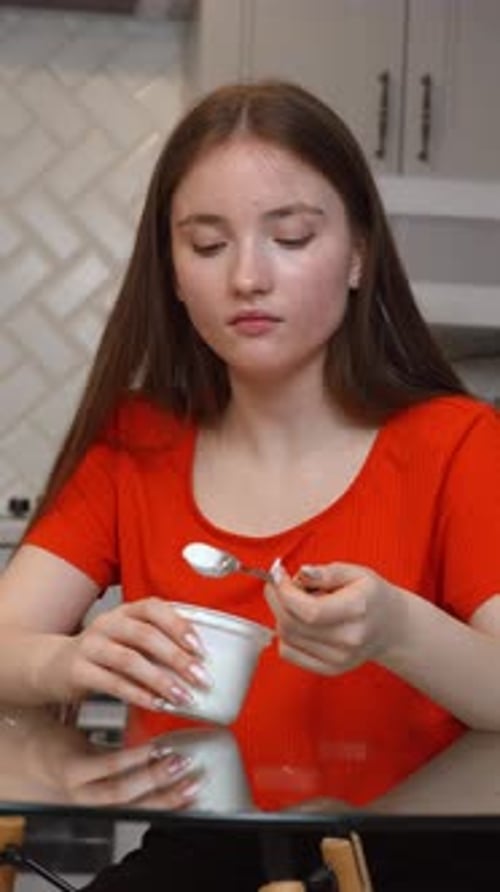 Young Woman Eating Yogurt at Kitchen Table