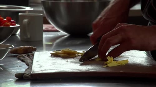 Un cuisinier tranche des brins de racine de gingembre frais en préparation d'un plat de restaurant