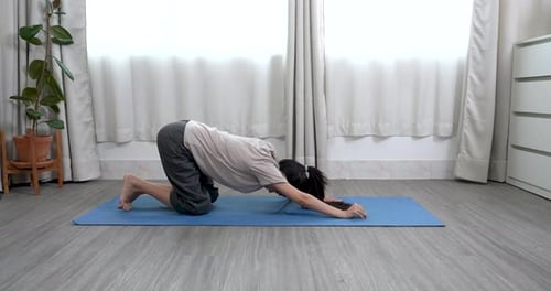 mulher asiática ajoelhada no tapete, estendendo suavemente os braços para a frente em pose de criança relaxando o corpo inteiro