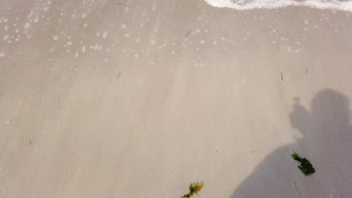 Schatten einer Person am Sandstrand mit einer Meereswelle.