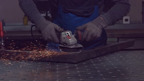 Factory Worker Grinds Metal Construction using angle grinder. Bright Golden Sparks comes out, Heavy
