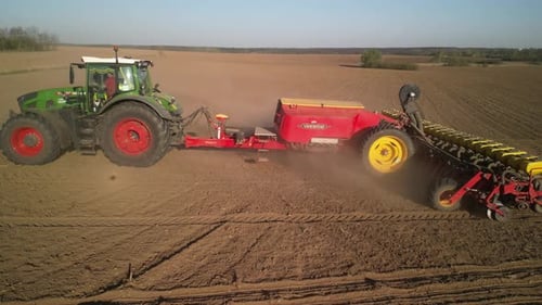 Green tractor works on the field sowing sunflower. Tractor planting corn in Ukraine
