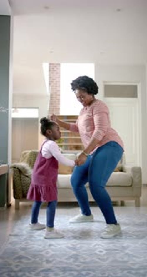 Vertical video of happy african american mother and daughter dancing at home, slow motion