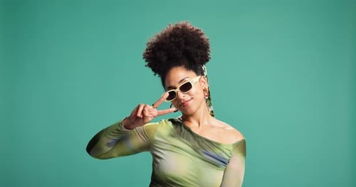 Face, peace sign and woman in studio, sunglasses and fashion on green background