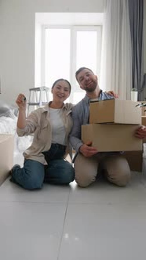 Happy Couple with Boxes Kneeling in New Home