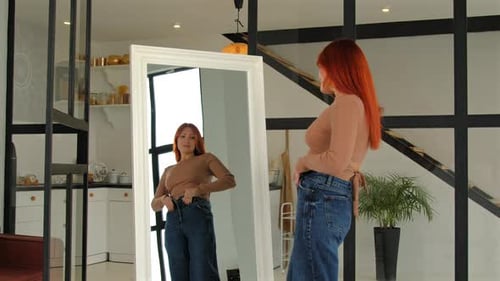 Displeased Middle Aged Woman Trying to Button Tight Denim in Front of Mirror