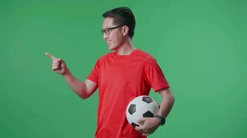Side View Of Asian Man With A Ball Putting Hand On His Chest And Pointing Forward On Green Screen