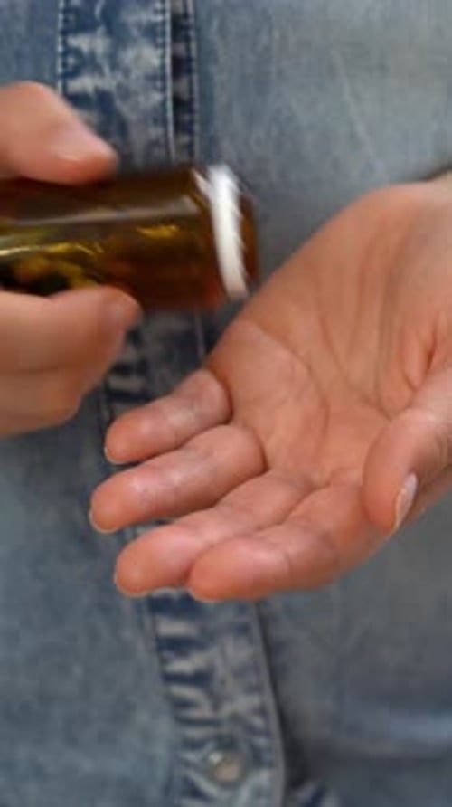 Woman Pours Green and White Capsules Into Hand