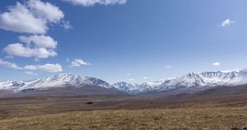 Timelapse of Sun Movement on Crystal Clear Sky with Clouds Over Snow Mountain Top Yellow Grass at