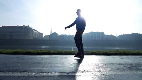 Silhouette of fit male jogger stretching legs near river in urban city park