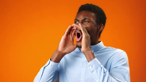 Young African Man Shouting Against Orange Background in Studio