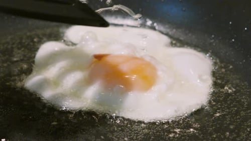In heißem Öl sprudelndes Spiegelei wird in Zeitlupe gespritzt, um Eigelb darauf zu kochen.