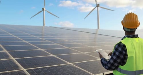Der junge Ingenieur verwendet ein digitales Tablet, um Sonnenkollektoren in einem Park für erneuerbare Energien zu inspizieren