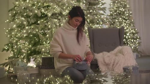 Young Woman Opening Christmas Gift in Cozy Home