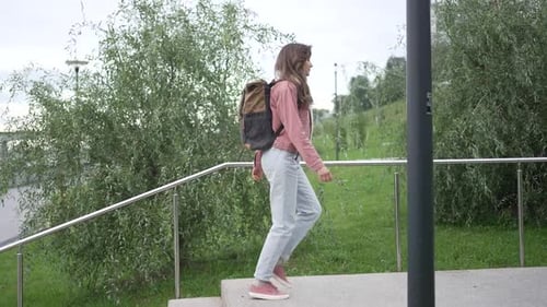 Young Woman with a Backpack Strolls Up and Down Stairs in an Urban Park Relishing the Fresh Air and