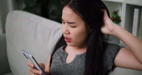 Frustrated Woman Using Smartphone on Couch Indoors