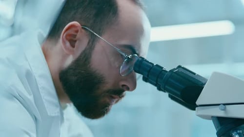 Bearded Man Uses Microscope in Brightly Lit Lab