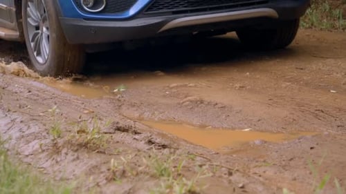 Car passing through a dirt road, navigating through a mud puddle.