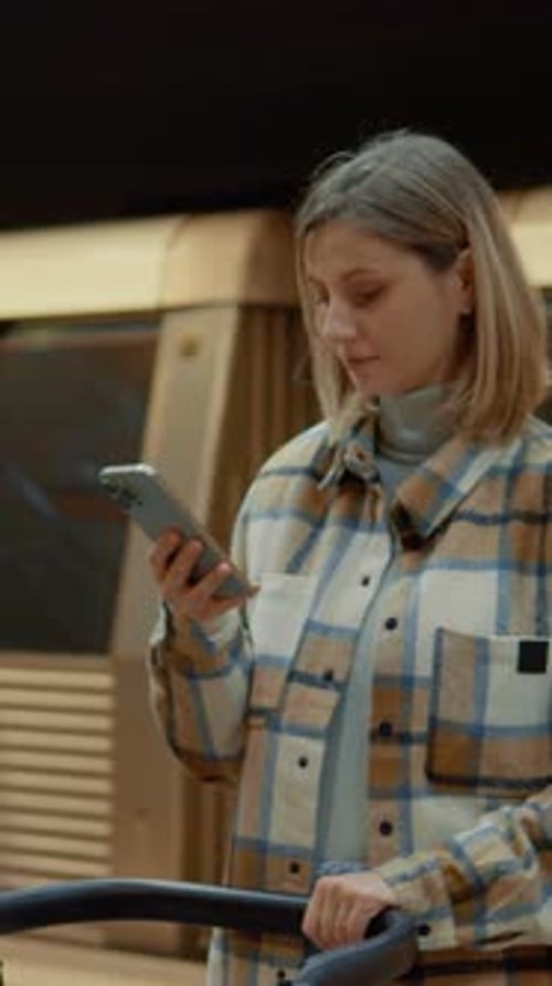 Vertical Screen Mother using smartphone while waiting for subway with stroller