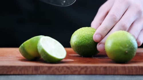 Chef with sharp knife cuts fresh green lime lemon on wooden cutting board