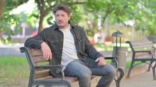 Man Sits on a Bench in a Sunny Park