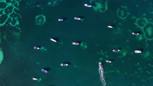 Top down aerial view of a speedboat smoothly moving between other moored boats in shallow waters. Mo