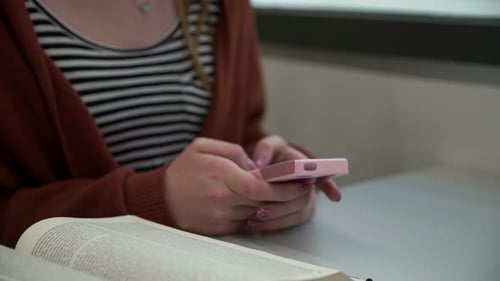 Young woman using phone at desk with book