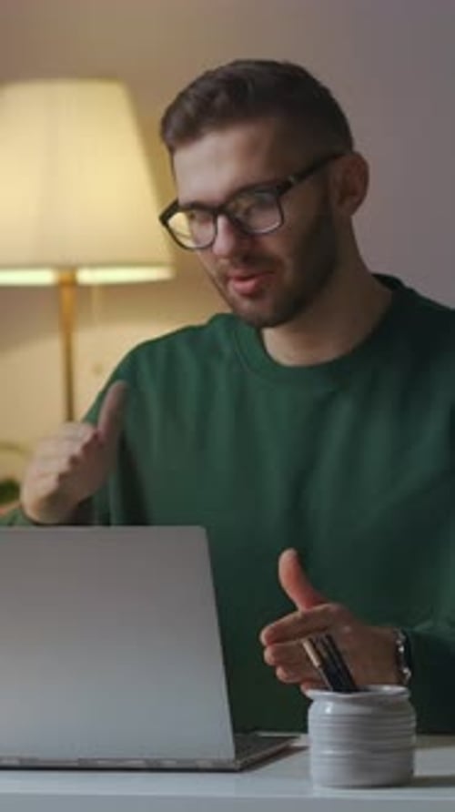 Un jeune homme à lunettes communique et fait des gestes avec enthousiasme tout en travaillant sur un ordinateur portable dans un