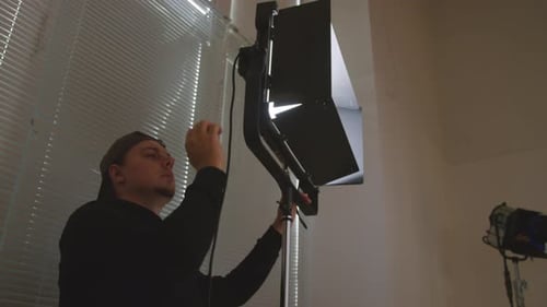 Caucasian Light Technician Installing Lamp on Tripod in Studio