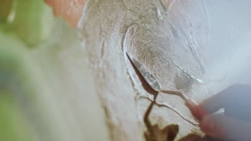 Nahaufnahme der Hand eines Künstlers, der mit einem Spachtel Farbe auf Leinwand verteilt