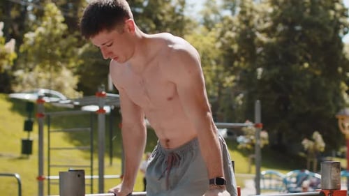 Athletic Caucasian Topless Man Practicing Dips on Parallel Bars Training Triceps on Playground