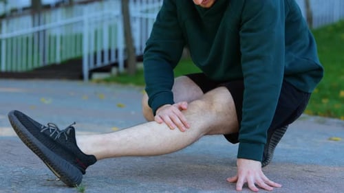 Sportsman Sitting and Stretching His Knee Leg Muscles in Green Park Young Caucasian Man Suffering