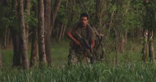 Man Walks with Rifle Through Forest During Day