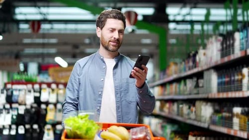 Handsome middle aged man buyer customer checking shopping list using smartphone, purchasing in groce