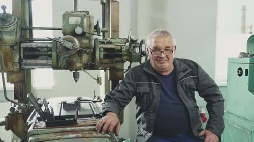 Older man resting next to vintage milling machine