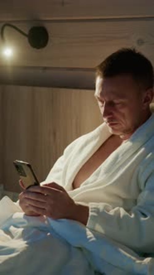 Soirée relaxante dans une chambre confortable avec un homme qui vérifie son téléphone dans un peignoir