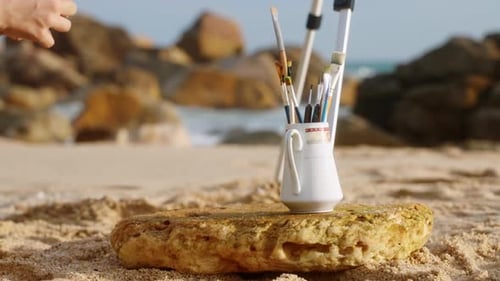 Artistic Woman Prepares Painting Tools on Sunny Sea Beach Canvas Stands on Shore Brushes Palette Oil