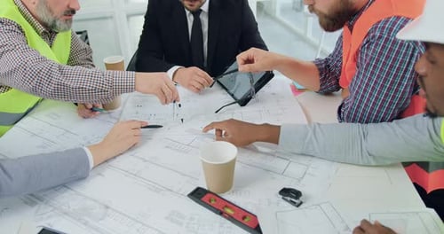 Nahaufnahme eines Ingenieurteams, das über ein Bauprojekt brainstormt und die Zeichnung auf dem Tisch vergleicht