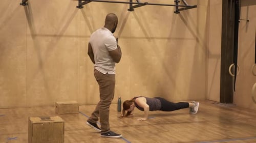 Un entraîneur personnel regarde une femme faire des burpees au gymnase pour se remettre en forme et s'améliorer
