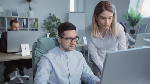 Attractive Man and Woman Talking Use Computer Working Together in a Modern Office On Background