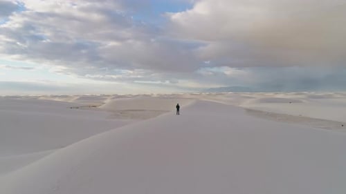 4K aerial passing over person revealing beautiful white sand dune field sunrise