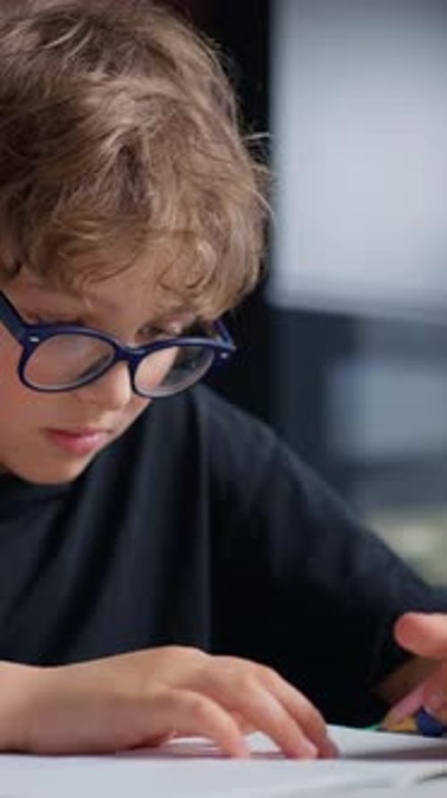 Young Boy with Curly Hair and Glasses Wearing a Black Shirt Intently Focused on Reading or Writing