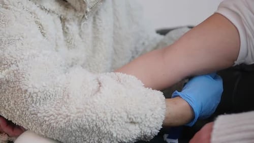 A nurse applies a tourniquet to a patient's arm during a home visit before taking a blood sample.