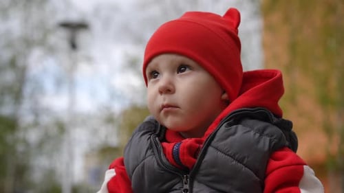Ralenti, gros plan, un regard attentionné et attentionné d'un petit garçon dans un bonnet rouge pour enfants assis
