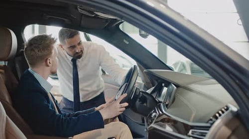 Man Trying out New Car in Dealership and Salesman Explaining its Features