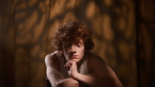 Chest-up Portrait of Curly-Haired Young Man Leaning on Chair Back with Arms