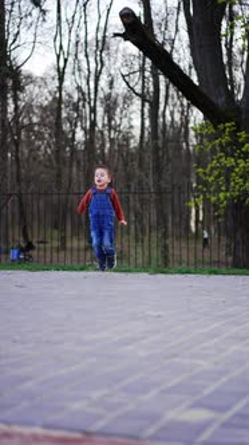 Cheerful Caucasian toddler in jeans romper jumps happily.