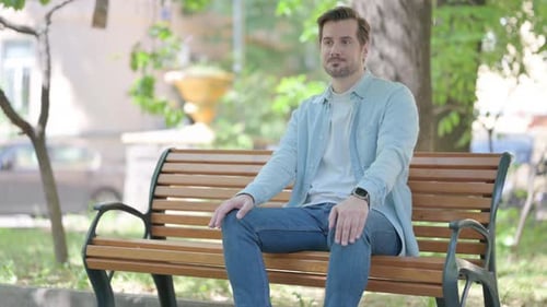 Man Sits on Park Bench Checking Smartwatch